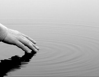 hand gently touching water in pond and making ripples