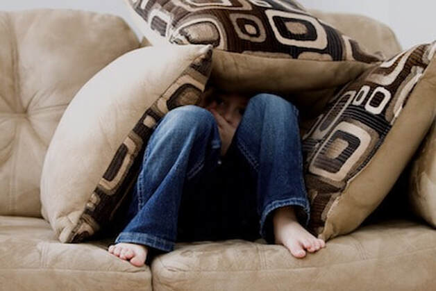 Little kid sitting on couch covered with pillows photo by ambermbPicture